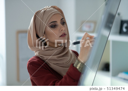 Young Muslim teacher standing near whiteboard and writing on it 51349474