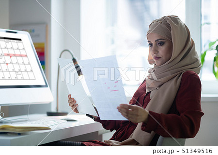 Dark-eyed teacher wearing hijab sitting near computer Dark-eyed teacher wearing hijab sitting near computer 51349516