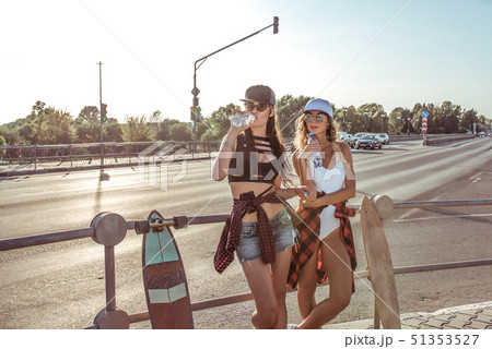 Two women girlfriends, stand road intersection, skate, drink water from bottle, longboard, free Two women girlfriends, stand road intersection, skate, drink water from bottle, longboard, free 51353527