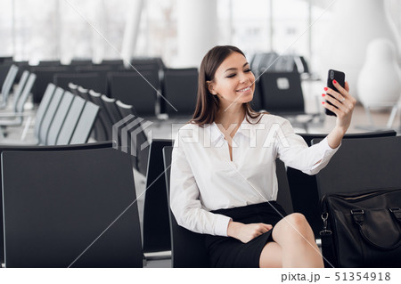 Young business woman at international airport, making selfie with mobile phone and waiting for her Young business woman at international airport, making selfie with mobile phone and waiting for her 51354918