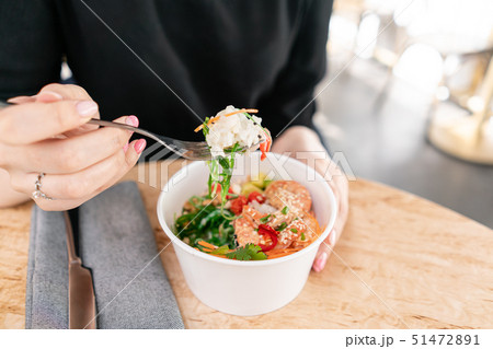 Woman eating traditional Hawaiian dish poke bowl with fork. Shrimps with rice, radish,cucumber Woman eating traditional Hawaiian dish poke bowl with fork. Shrimps with rice, radish,cucumber 51472891