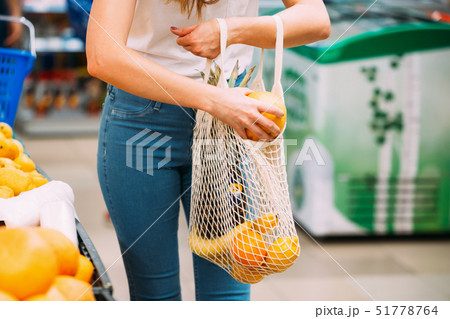 Woman with mesh bag full of fresh vegetables shopping at the store, zero waste concept Woman with mesh bag full of fresh vegetables shopping at the store, zero waste concept 51778764