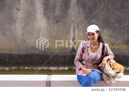 Portrait of young beautiful Asian woman sitting outdoors Portrait of young beautiful Asian woman sitting outdoors 52394596