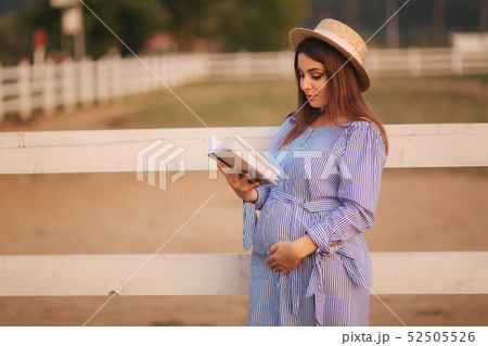 Beautiful pregnant woman read the book on the farm. She stand by the fance and look in to the book Beautiful pregnant woman read the book on the farm. She stand by the fance and look in to the book 52505526