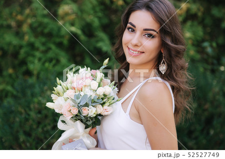 Gorgeous female in white dress slime. Beautiful girl hold a bouquet of flowers in hands Gorgeous female in white dress slime. Beautiful girl hold a bouquet of flowers in hands 52527749