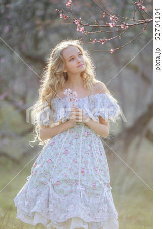 Cute girl in a long dress, walking through the park with flowers in hands 52704104