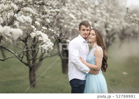 Young couple in love resting in the blooming garden. white blooming trees Young couple in love resting in the blooming garden. white blooming trees 52799991