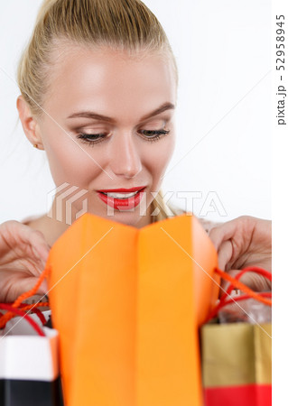 Blond woman inspecting content of colored paper bags Blond woman inspecting content of colored paper bags 52958945
