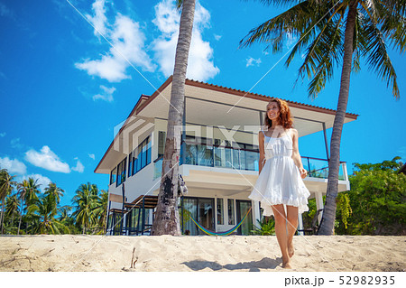 Beautiful slim girl walking on a beautiful tropical beach on the background of a luxury villa Beautiful slim girl walking on a beautiful tropical beach on the background of a luxury villa 52982935