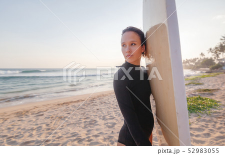 Young beautiful woman with a surfboard on the ocean with a surfboard in the rays of t Young beautiful woman with a surfboard on the ocean with a surfboard in the rays of t 52983055