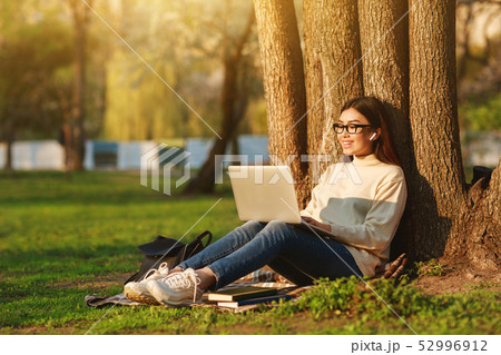 Student Girl Using Laptop Sitting Under Tree At University Campus 52996912