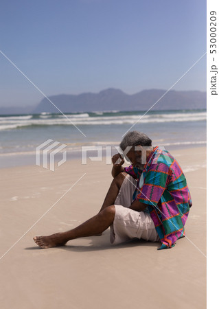 Senior man with hand on forehead sitting on beach 53000209