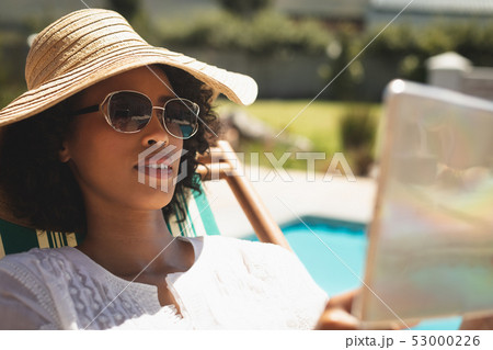 African American woman with hat and sunglasses using digital tablet in her backyard African American woman with hat and sunglasses using digital tablet in her backyard 53000226