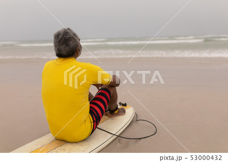 Senior male surfer sitting on the surfboard on beach Senior male surfer sitting on the surfboard on beach 53000432