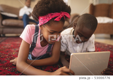 Close-up of African American sibling lying on floor and using digital tablet  53000776