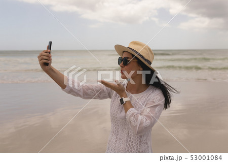 Young woman giving flying kiss while taking selfie with mobile phone 53001084