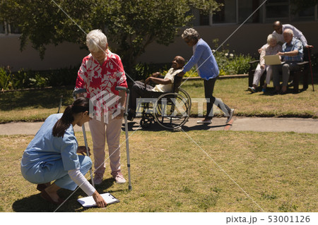Young female doctor examining disabled senior woman in garden Young female doctor examining disabled senior woman in garden 53001126