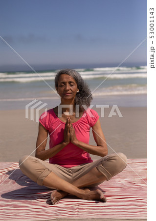 Senior woman with eyes closed and hands clasped doing yoga on beach Senior woman with eyes closed and hands clasped doing yoga on beach 53001143