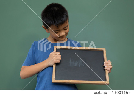 Smiling schoolboy standing and holding a hello slate in a classroom 53001165