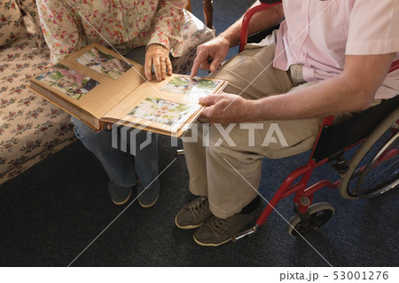 Senior couple looking at photo album in living room at nursing home Senior couple looking at photo album in living room at nursing home 53001276
