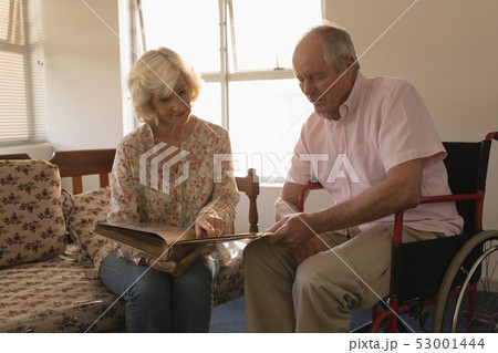 Senior couple looking at photo album in living room Senior couple looking at photo album in living room 53001444