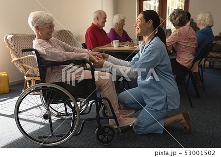 Side view of female doctor holding hands and talking with disable senior woman at home 53001502