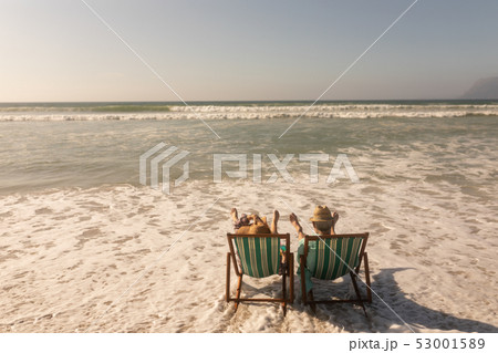 Senior couple relaxing together on sun lounger at beach 53001589
