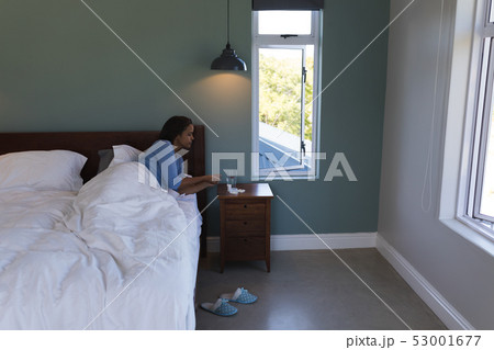Senior woman taking medicine with glass of water while lying in bed at home Senior woman taking medicine with glass of water while lying in bed at home 53001677