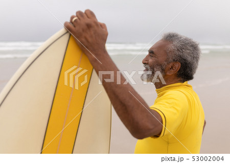 Senior male surfer standing with surfboard on the beach Senior male surfer standing with surfboard on the beach 53002004