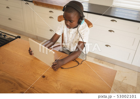 African American boy playing game on digital tablet at dining table in kitchen African American boy playing game on digital tablet at dining table in kitchen 53002101