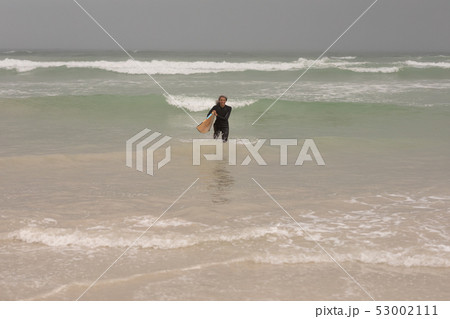 Senior female surfer with surfboard walking in the sea Senior female surfer with surfboard walking in the sea 53002111