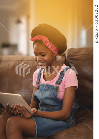 African American girl sitting on the sofa and using digital tablet African American girl sitting on the sofa and using digital tablet 53002252