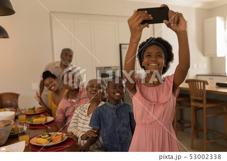 Girl taking selfie of family with mobile phone on dining table at home 53002338