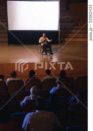 Businessman sitting on a wheelchair and giving presentation to the audience Businessman sitting on a wheelchair and giving presentation to the audience 53002432