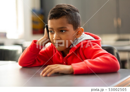 Schoolboy talking on mobile phone at desk in a classroom Schoolboy talking on mobile phone at desk in a classroom 53002505