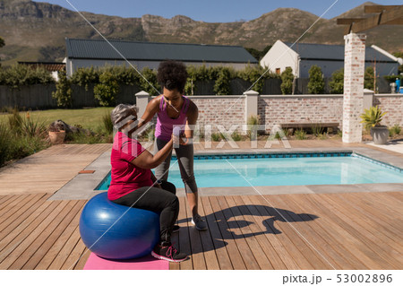 Female trainer training senior woman in performing exercise in the backyard 53002896