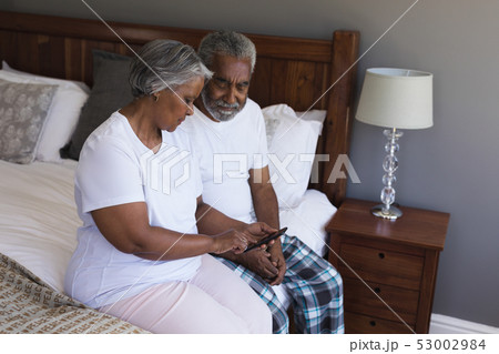 Senior couple using mobile phone in bedroom at home 53002984