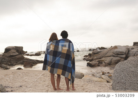 Caucasian couple wrapped in blanket standing at beach  53003209