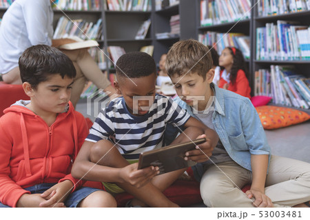 Schoolboys using a digital tablet while they are sitting on cushions in a library Schoolboys using a digital tablet while they are sitting on cushions in a library 53003481