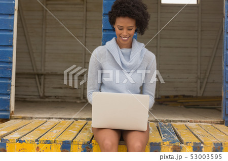Young African American woman using laptop at beach hut Young African American woman using laptop at beach hut 53003595
