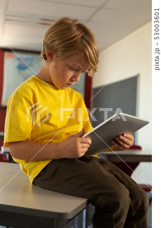 Boy sitting over desk and using digital tablet in a classroom Boy sitting over desk and using digital tablet in a classroom 53003601