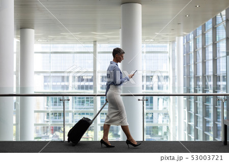 Caucasian businesswoman using mobile phone while walking in office Caucasian businesswoman using mobile phone while walking in office 53003721