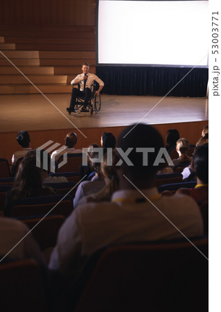 Businessman sitting on a wheelchair and giving presentation to the audience Businessman sitting on a wheelchair and giving presentation to the audience 53003771