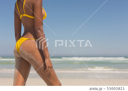 Young African American woman in yellow bikini standing on the beach 53003821