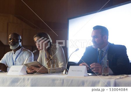 Businesswoman with executive speaking in speaker while sitting in the auditorium 53004084