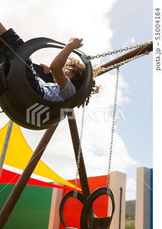 Schoolgirl playing in a swing swing in the school playground 53004164