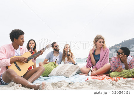 Man playing guitar while friends enjoying on beach Man playing guitar while friends enjoying on beach 53004535