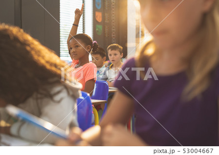 Schoolgirl raising hand while sitting in classroom 53004667