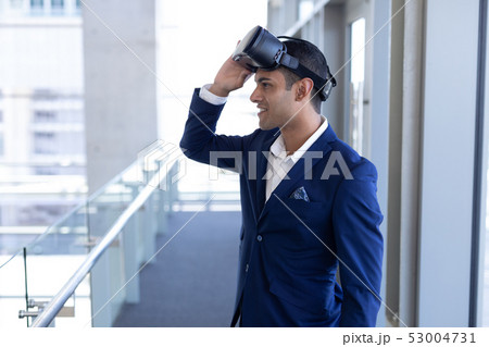 Mixed-race businessman using virtual reality headset standing in modern office 53004731