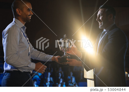 Businessman giving trophy to business male executive on stage in auditorium 53004844